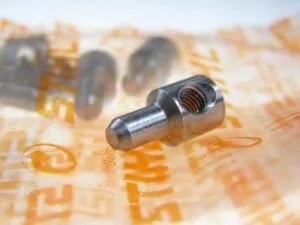 Nakrętka napinacza łańcucha STIHL 1120-664-1500 (napinacz czołowy). Widok nakrętki na oruginalnym opakowniu STIHL. W tle widoczne kolejne "rozmazane" nakrętki.